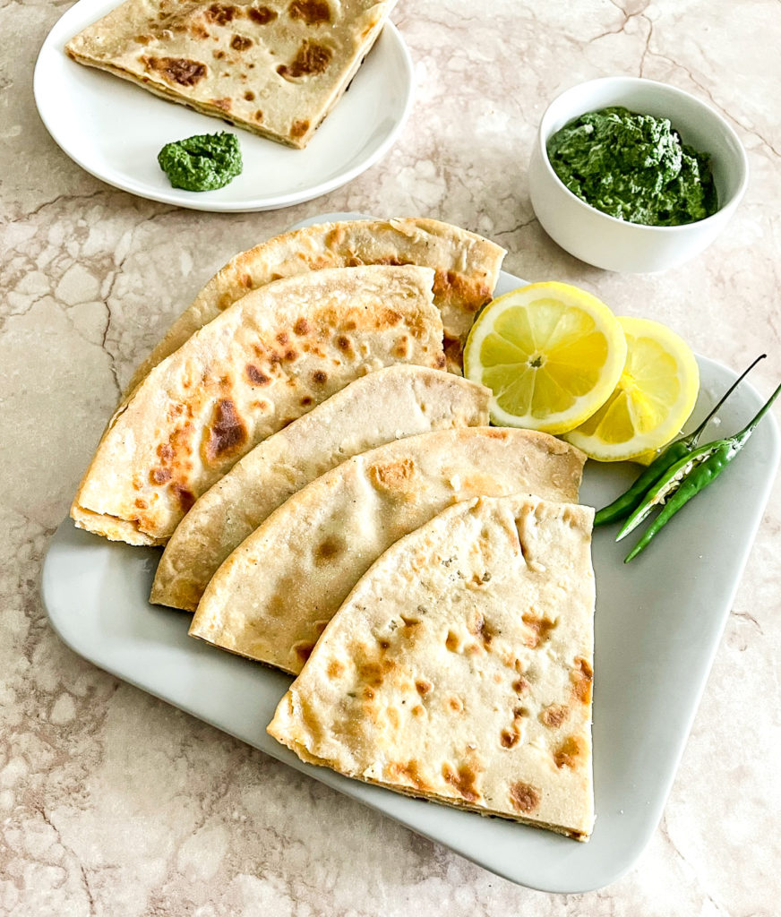 aloo paratha cut up into quarters on a plate with lemon and chilli