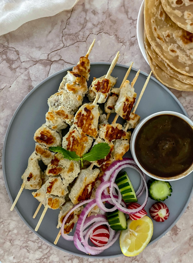 chicken malai boti skewers on a plate with vegetables and imli (tamarind) chutney