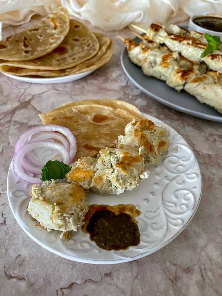 chicken malai boti on a plate with imli (tamarind) chutney, onions and paratha