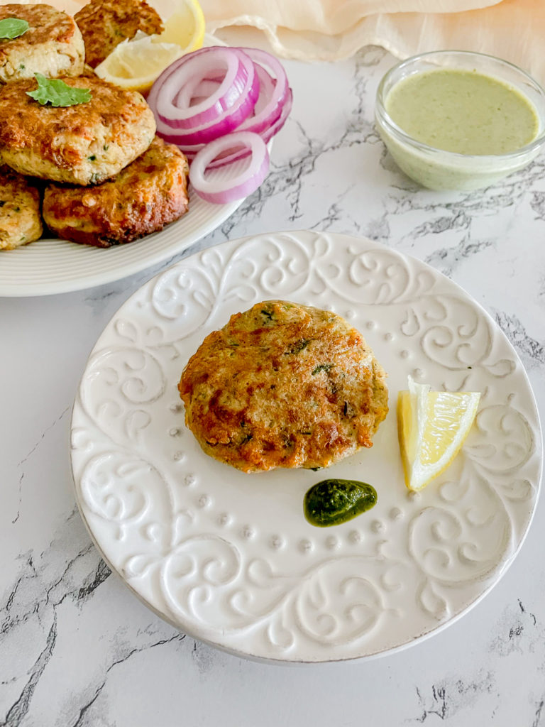 one chicken shami kabab on a plate with lemon and green chutney