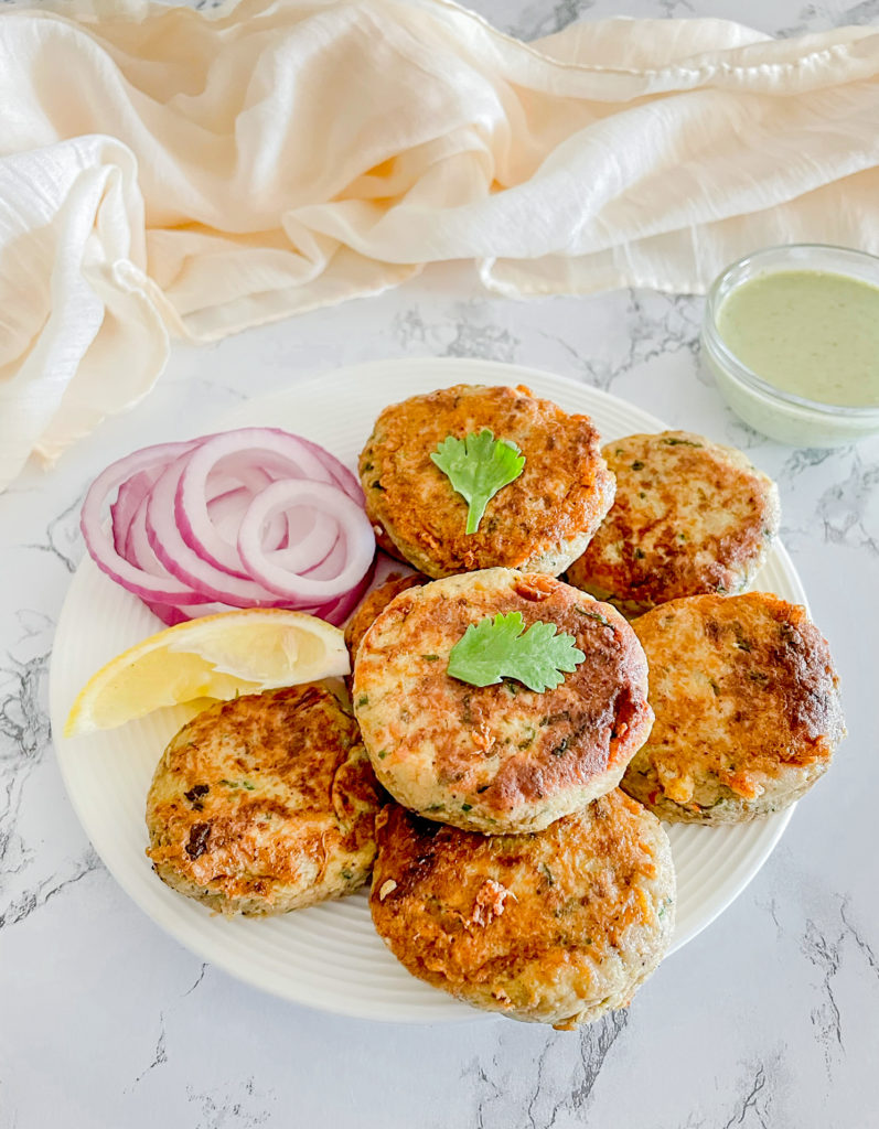 plate of chicken shami kabab garnished with lemon and onions