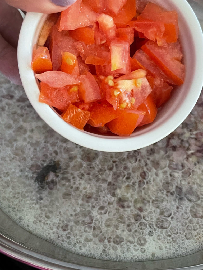 adding tomatoes to a pot for rajma curry