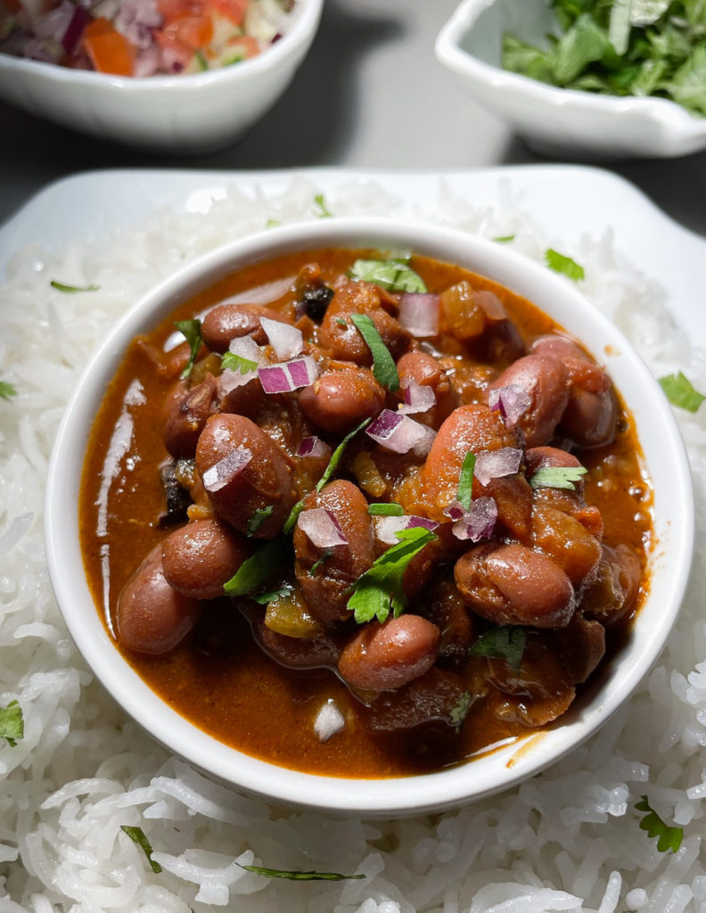 rajma curry in a small bowl with a plate of rice