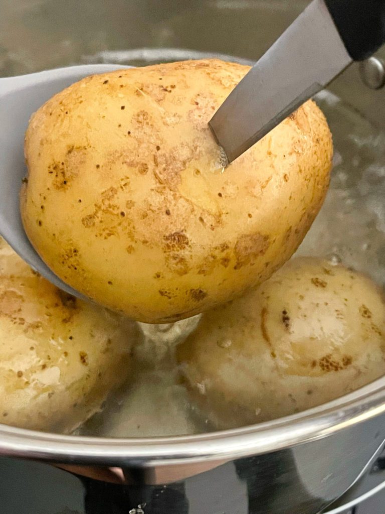 potatoes boiling in pot with knife poked in one