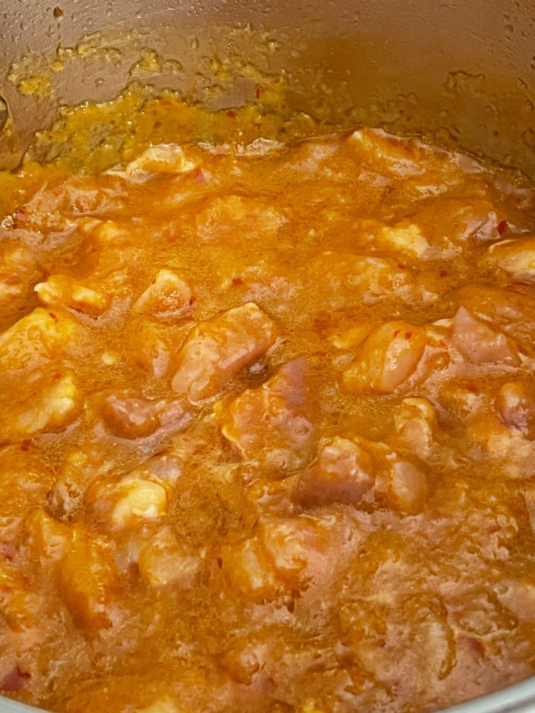 chicken being cooked in pot of sauce